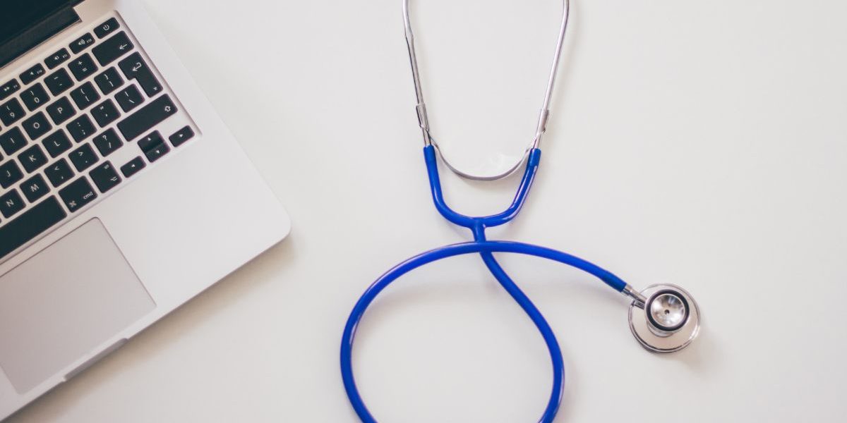 laptop and stethoscope laying on a white surface