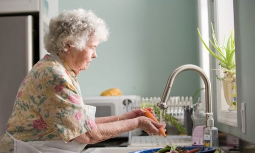 old woman washing carrots in sink