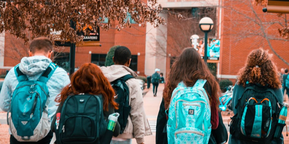 Group of high schoolers with backpacks walking towards school building
