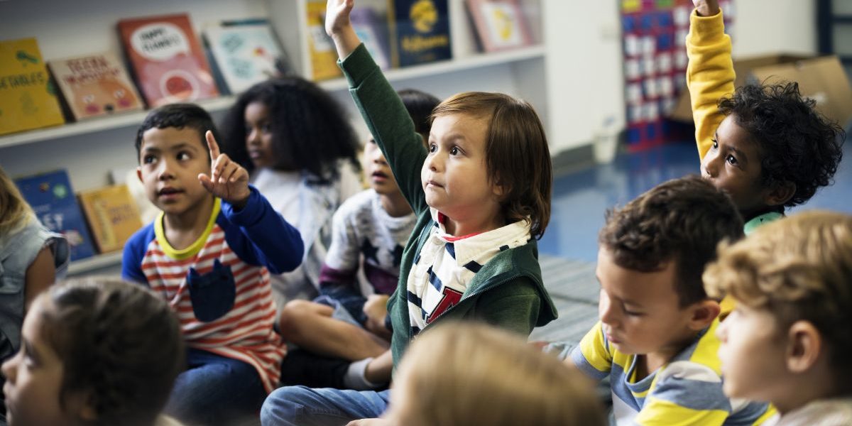 group of children in classroom raising hands