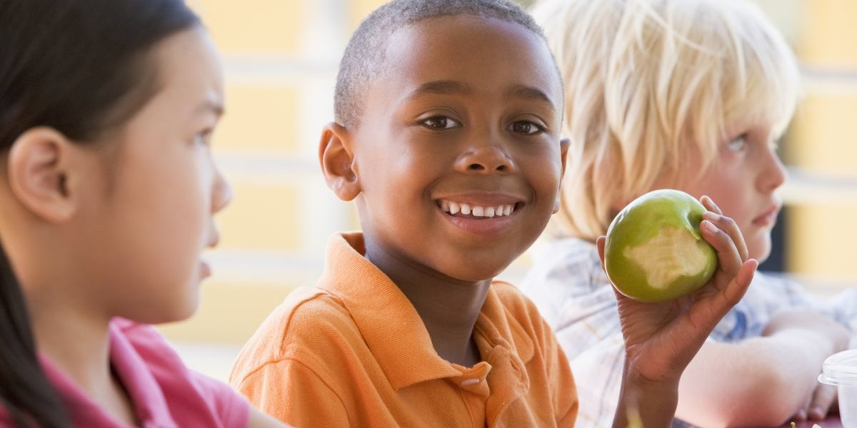 close up of three kids with one eating an apple