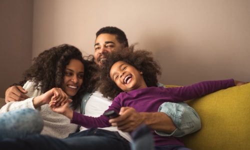 woman, man, and child sitting on couch hugging and laughing