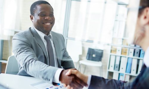 two people in business attire shaking hands across a desk