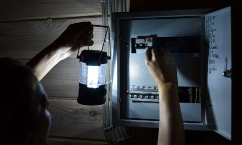 person holding a lantern and working on a breaker box