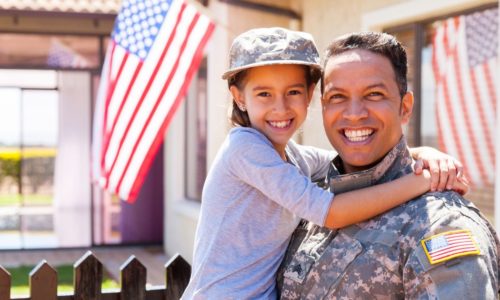 veteran holding child in front of house